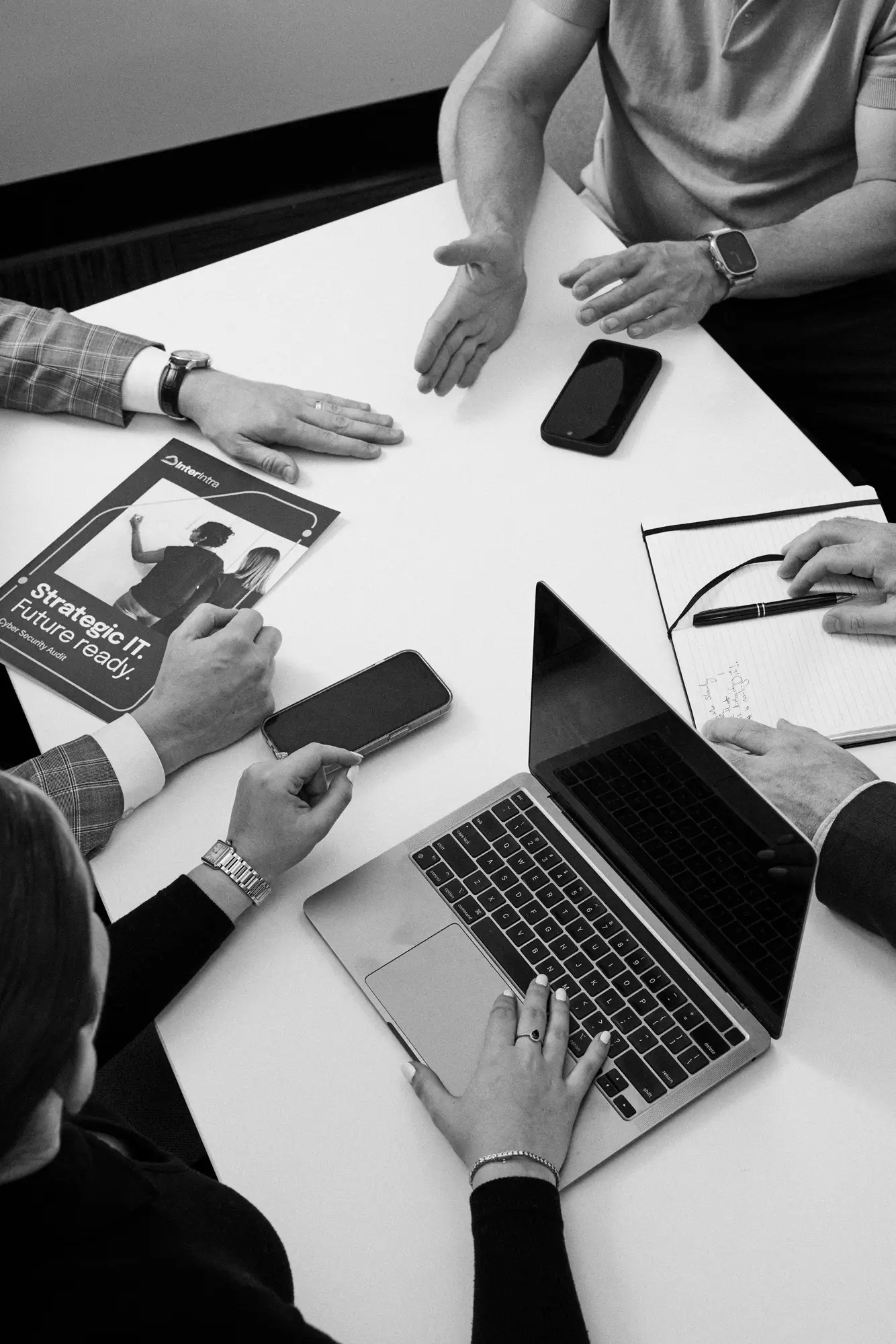 A laptop and some phones on a desk while people are in a meeting